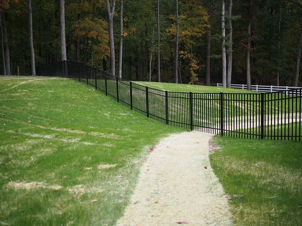 Black aluminum fence following a grassy slope beside a gravel path
