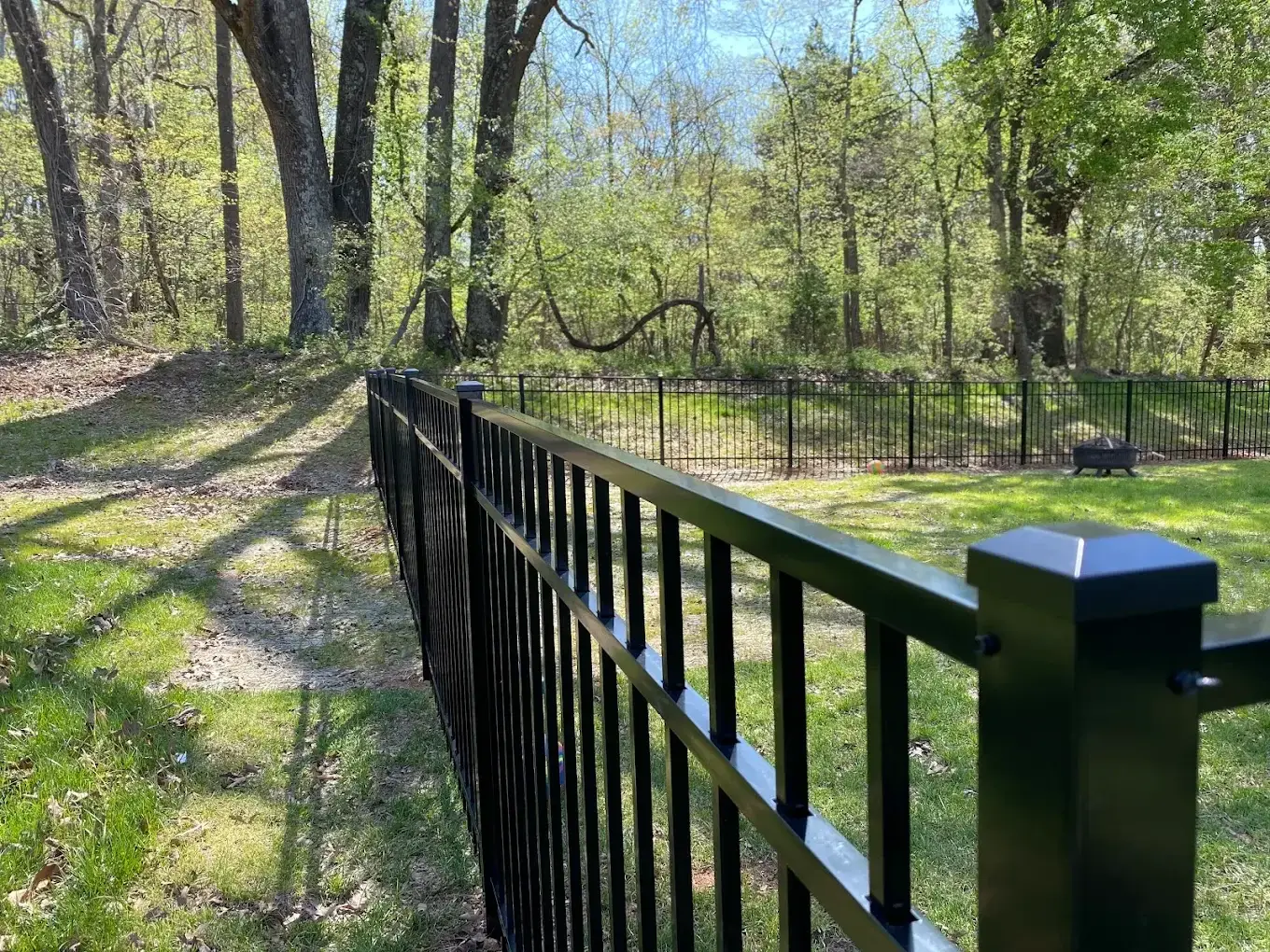 Black aluminum fence following a lawn beside mature trees
