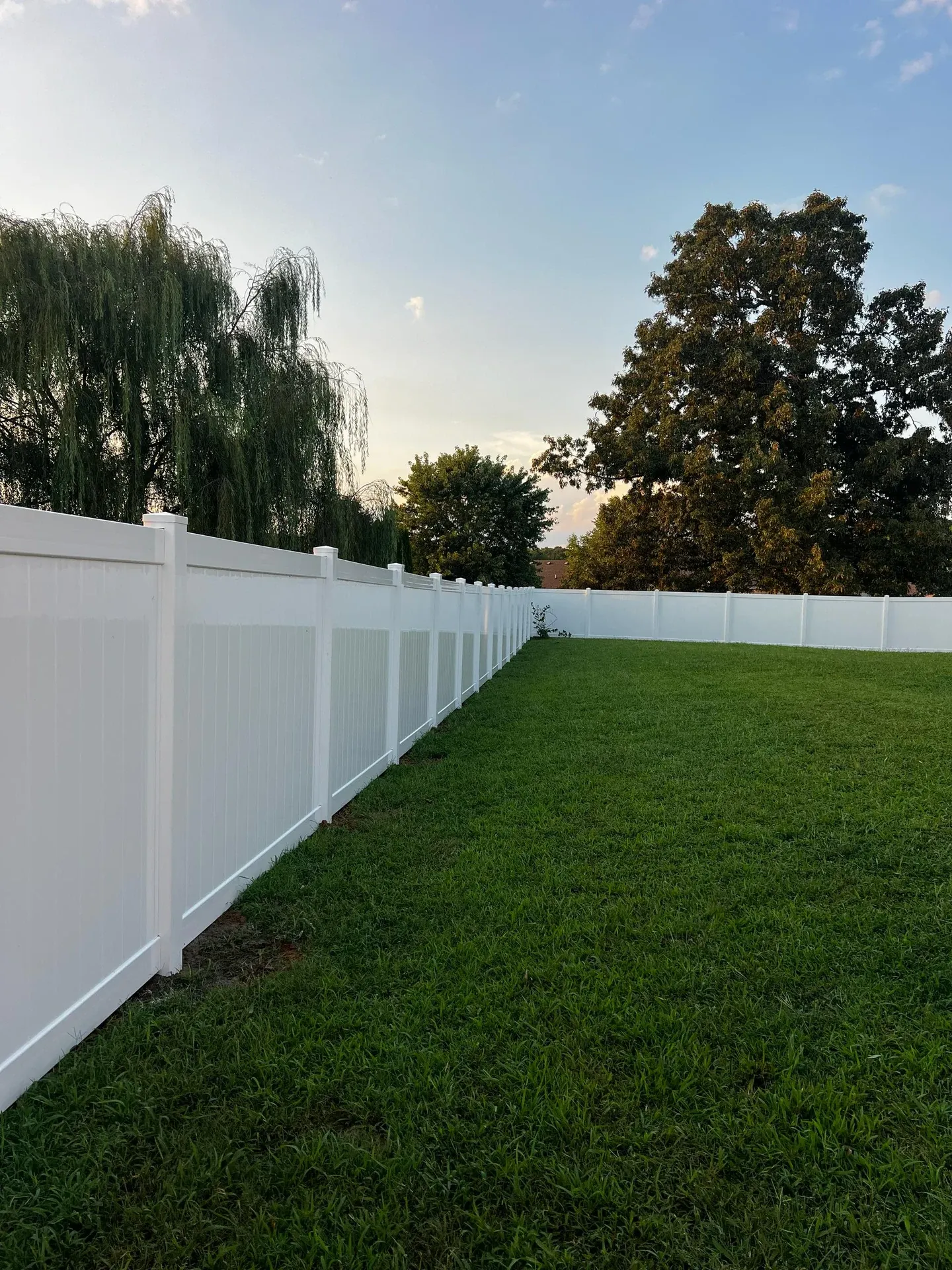 White vinyl privacy fence corner and long lawn at dusk