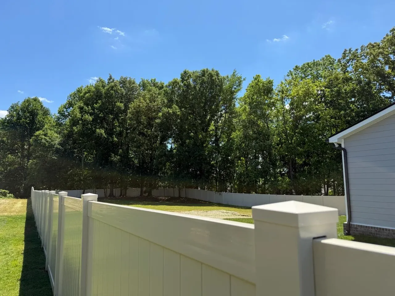 White vinyl fence posts and top rail along a sunny backyard