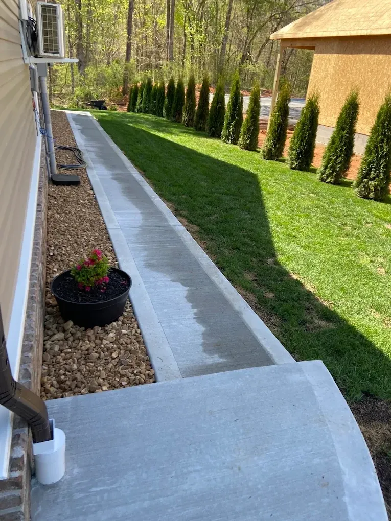 Concrete side-yard walkway between a house and landscaped lawn