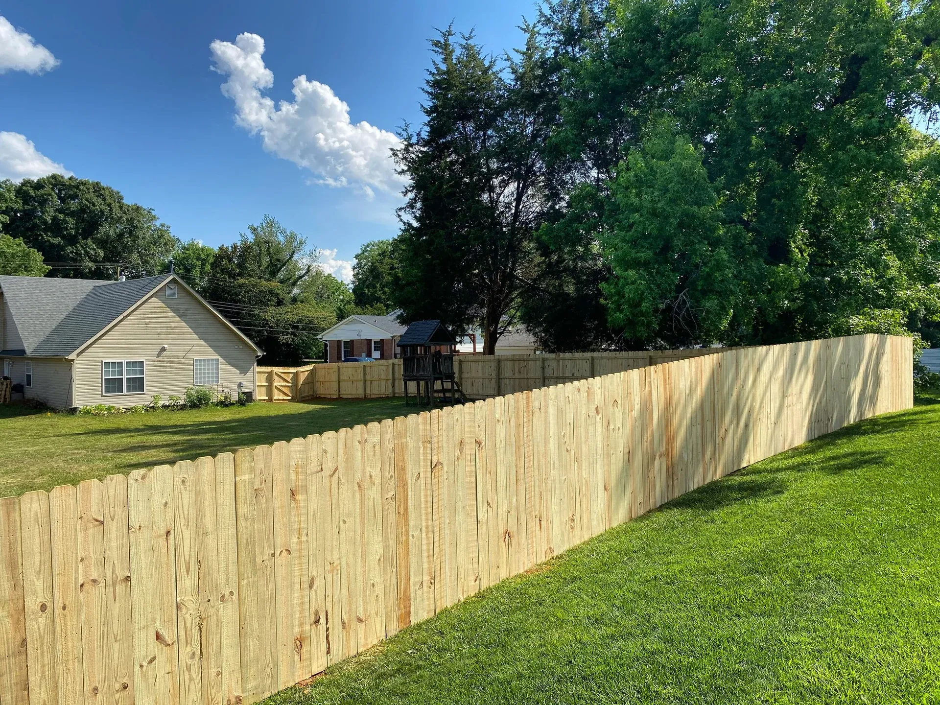 Wood privacy fence following a green lawn beneath a blue sky